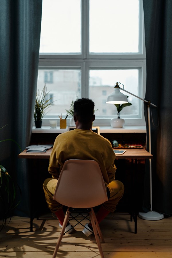 Un étudiant en pull jaune révise à son bureau devant une fenêtre